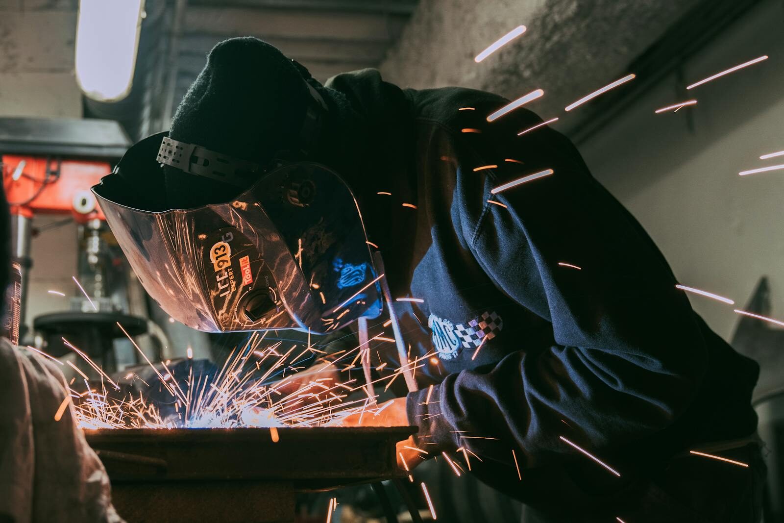 Skilled welder working indoors, generating bright sparks, wearing safety gear.